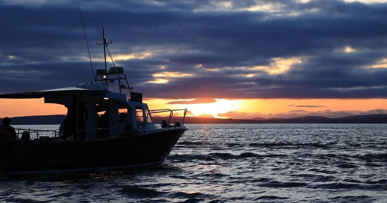Sunset boat silhouette on open ocean, evening fishing excursion