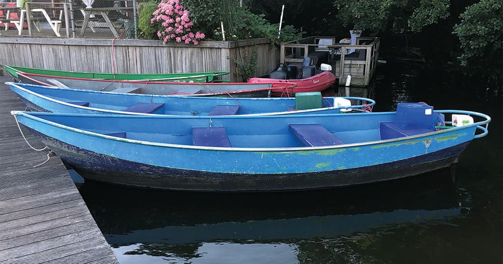 Blue rental rowboats docked at a calm marina by trees