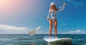 Woman paddleboarding under sun on calm ocean, scenic tour