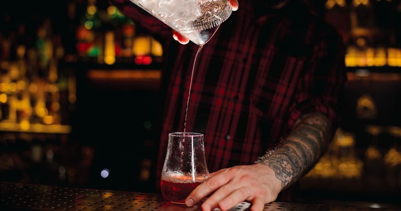 Bartender pouring cocktail behind dimly lit indoor bar counter