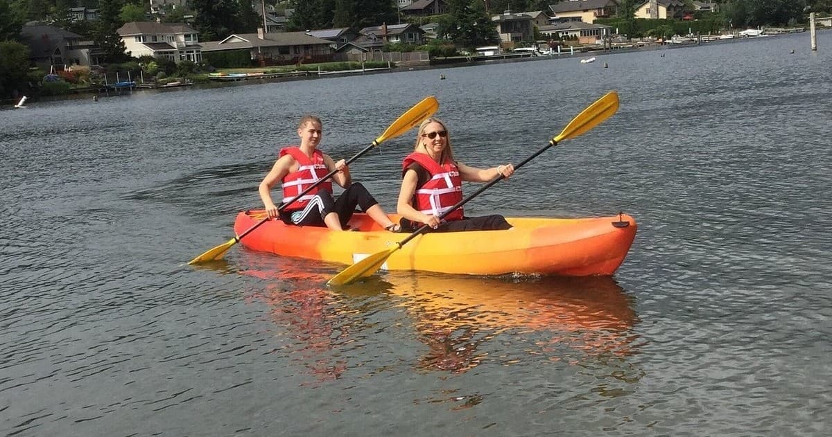 Two kayakers paddling tandem on suburban calm lake