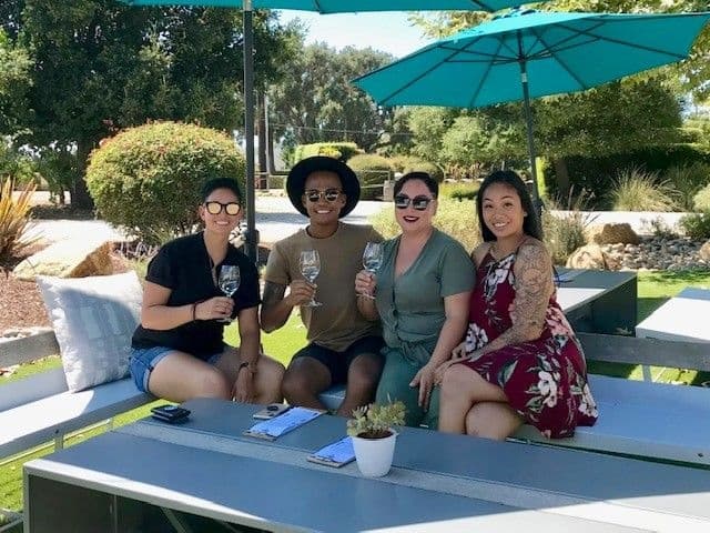 Friends enjoying outdoor wine tasting at shaded picnic table