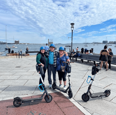 Three riders posing with electric scooters on waterfront promenade