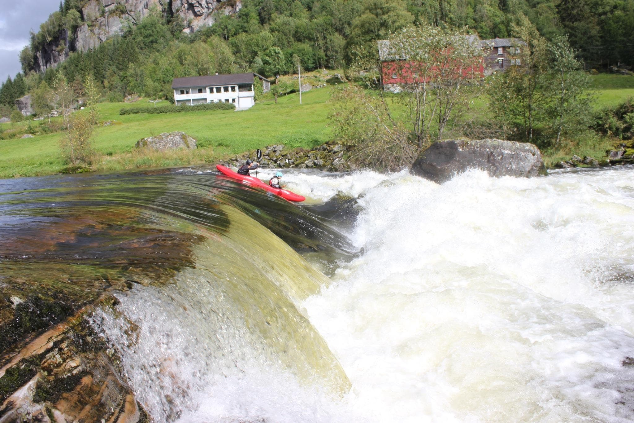 Whitewater kayaker dropping over a waterfall in green valley
