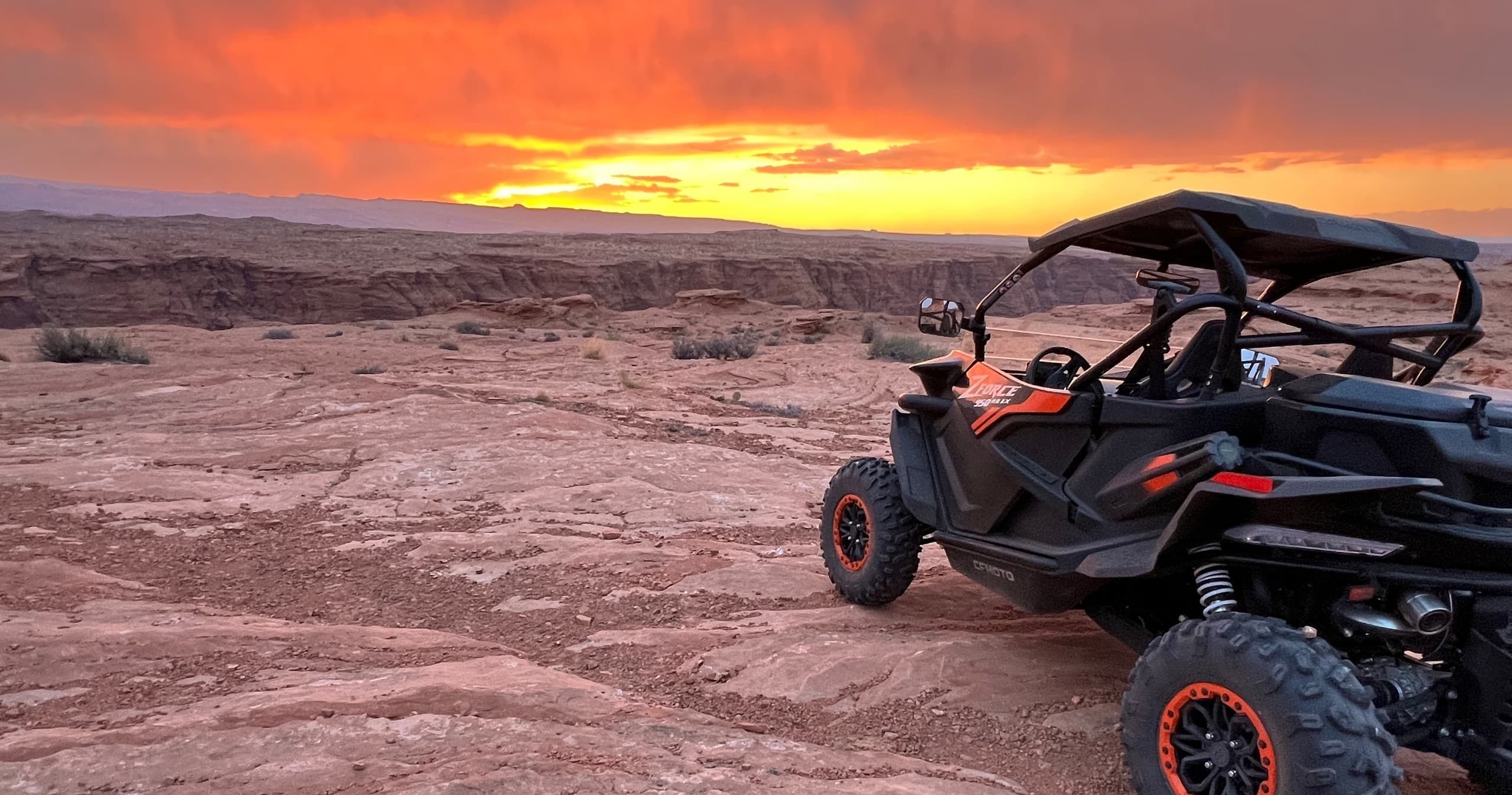 Rugged UTV parked on sandy beach with dramatic sunset sky