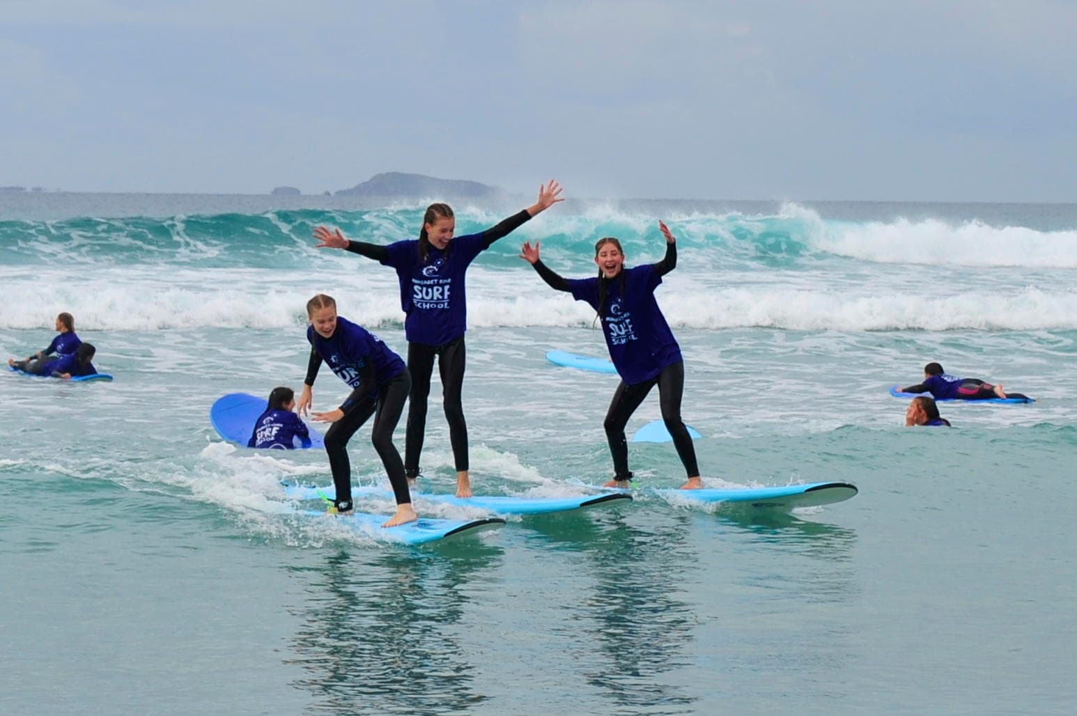 Three surfers balancing on one longboard in shallow surf at Margaret River