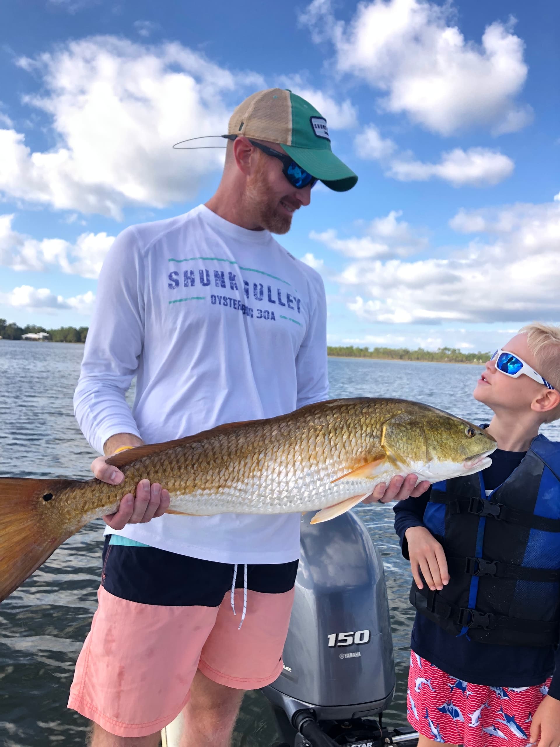 Father and child holding redfish on boat near shoreline