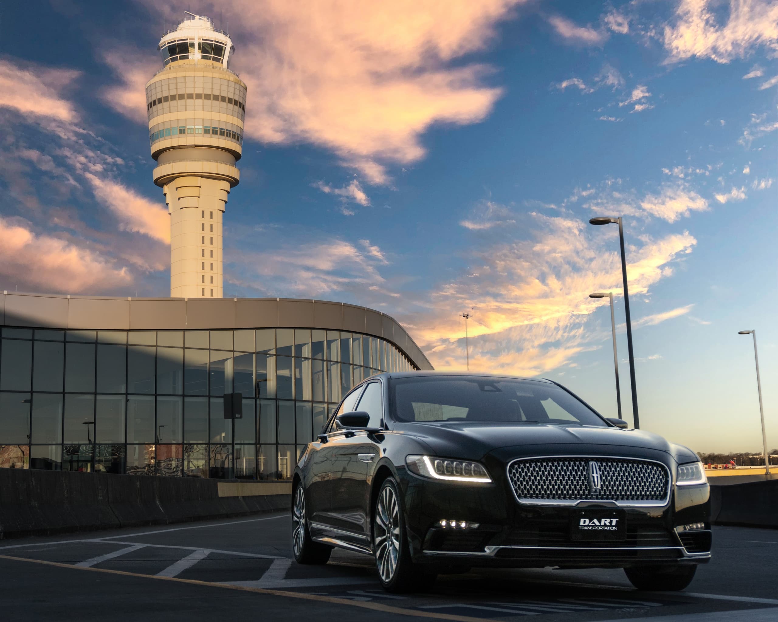 Luxury sedan parked near airport control tower at golden sunset
