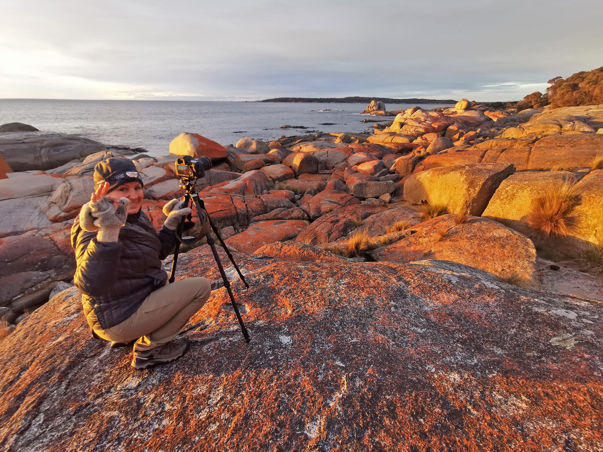 Photographer shooting sunrise on rocky coastline with tripod