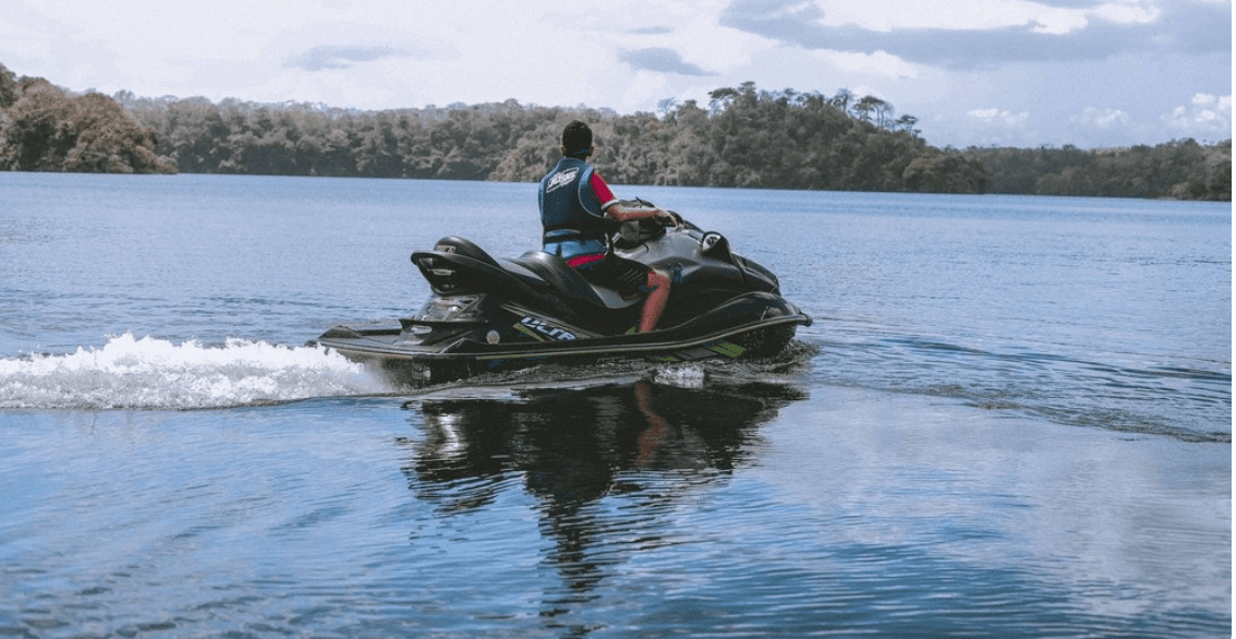 Rider cruising jet ski on calm lake near coastal tree line