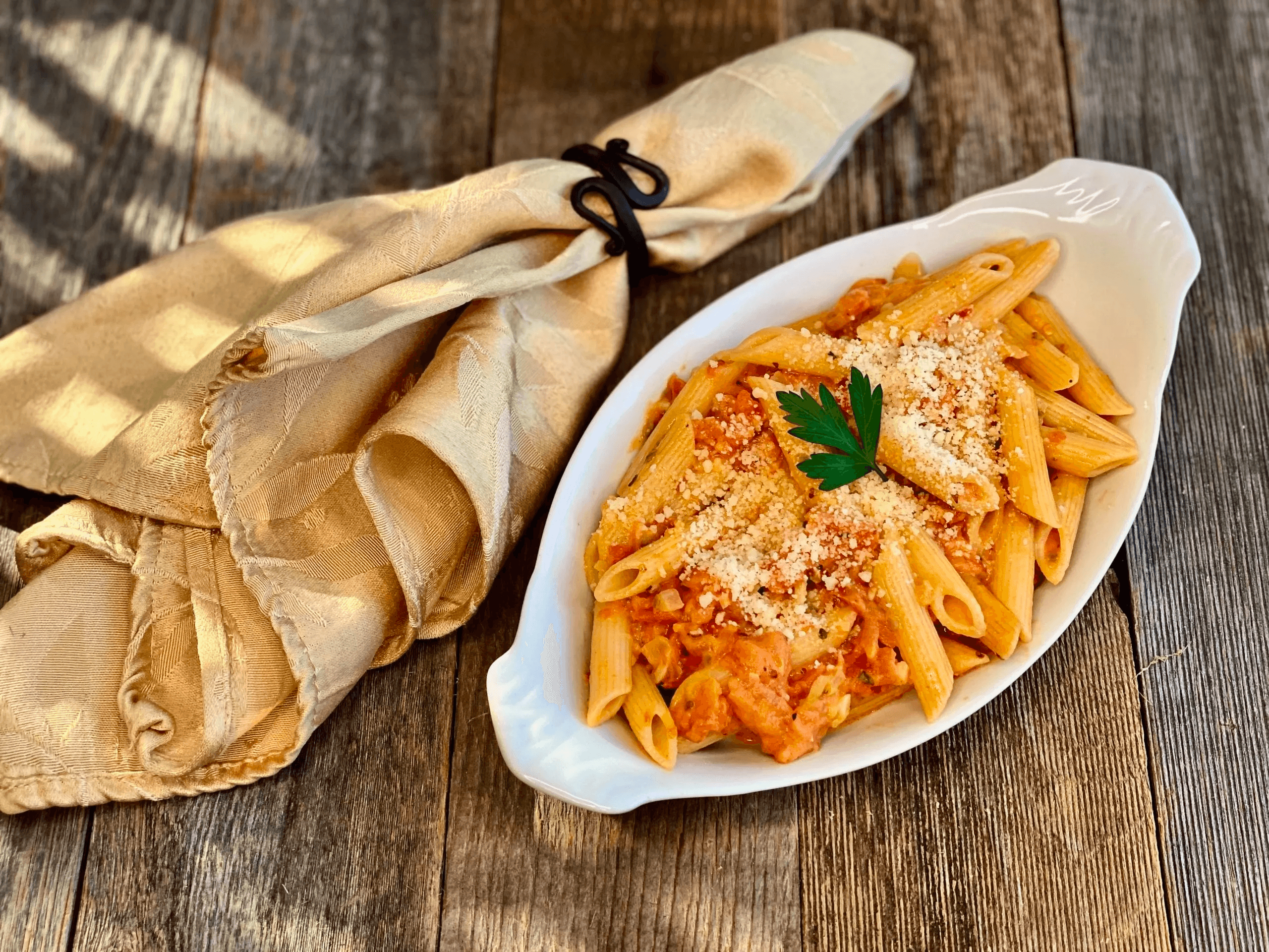 Baked penne pasta in oval dish on wooden board, comfort meal