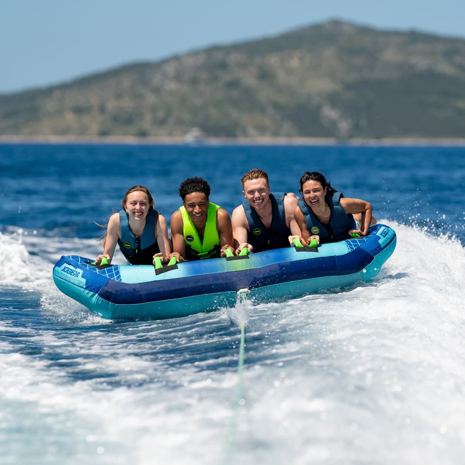 Four riders on inflatable tow tube over blue sea, high-speed tow