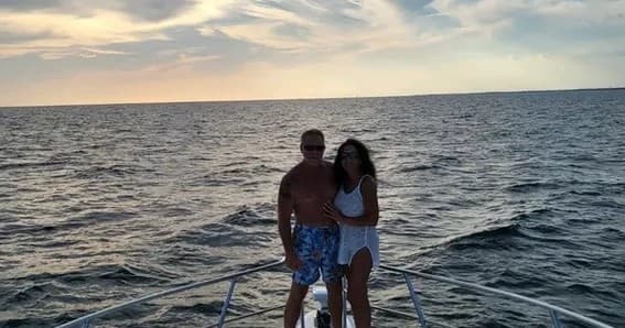 Couple posing on yacht bow at sunset over open ocean
