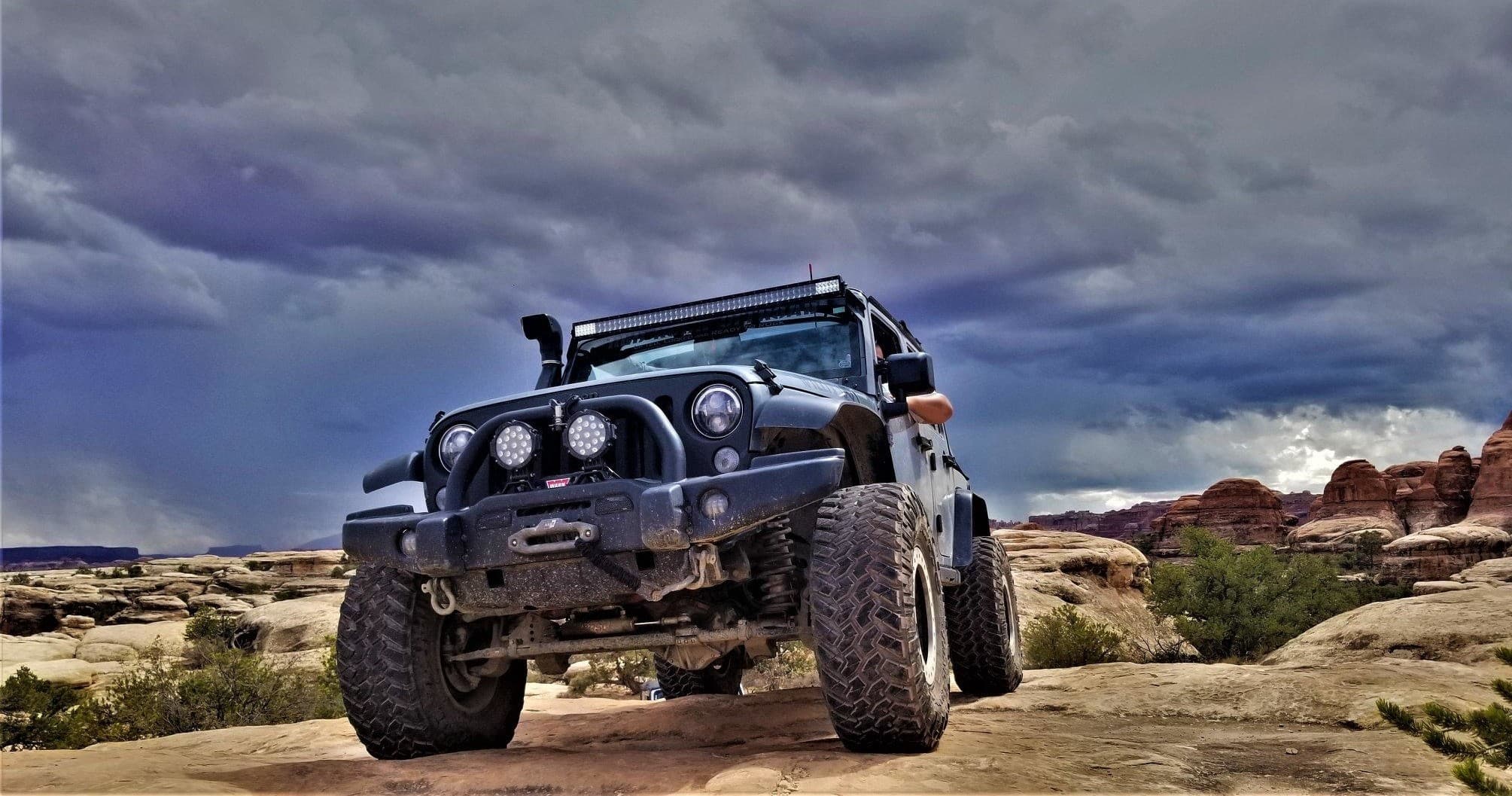 Lifted Jeep perched on sandstone ledge under dramatic cloudy sky