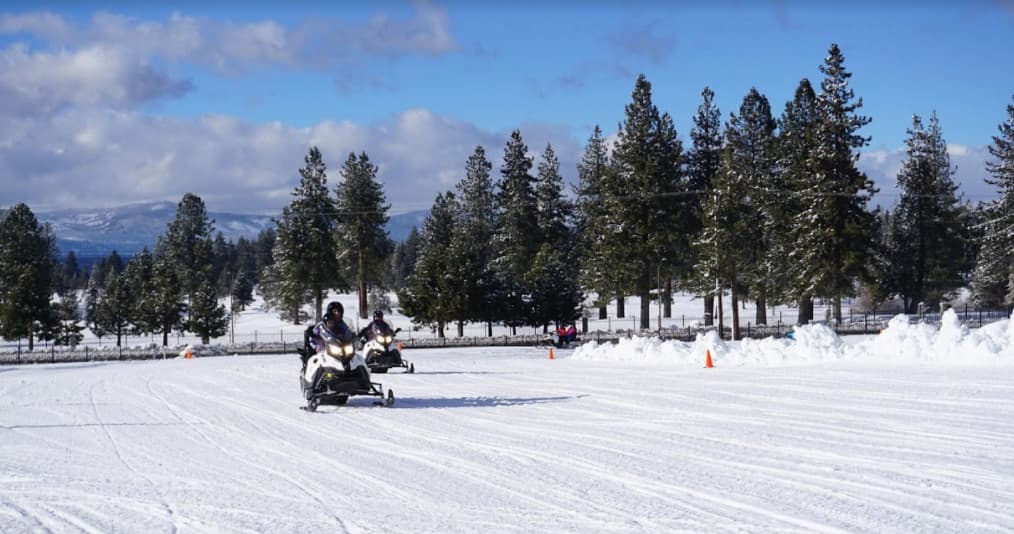 Guided snowmobile convoy traversing snowy plain under blue skies