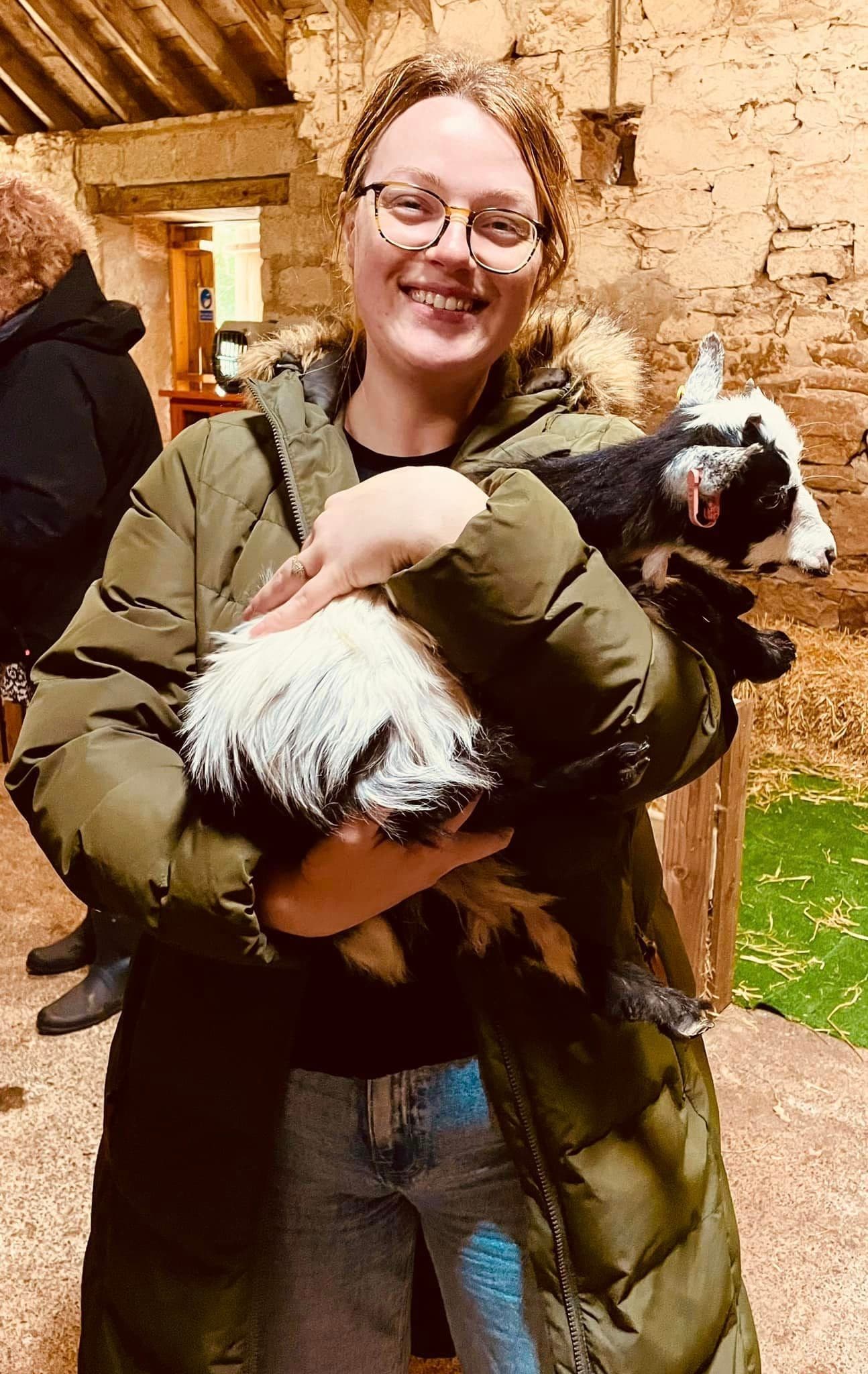 Visitor holding baby goat inside rustic barn during farm visit