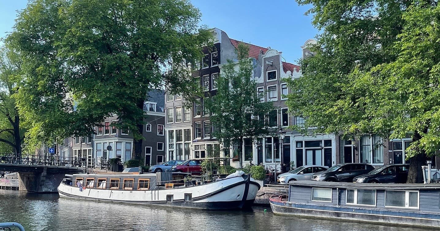 Amsterdam canal boat tour past historic canal houses and trees