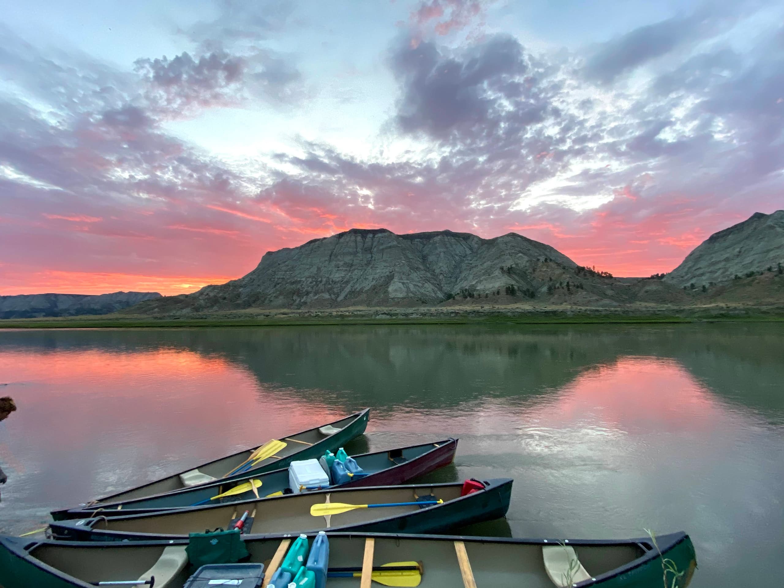 Canoes lined on reflective lake at sunset, mountain scenery