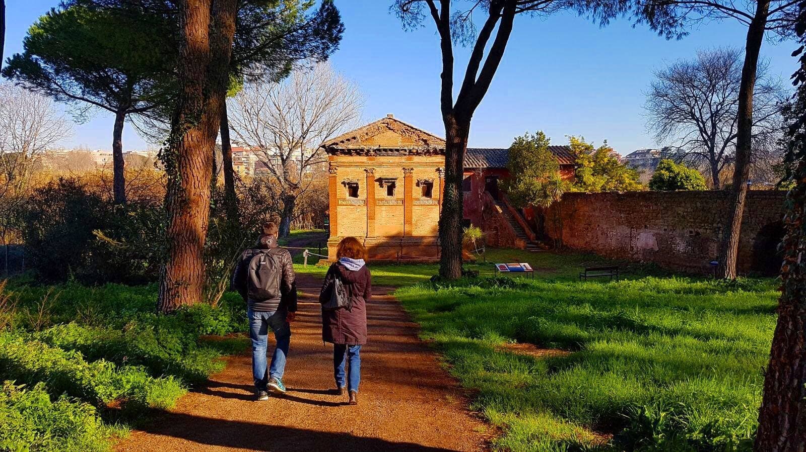 Walkers exploring grassy Roman ruins path near small temple