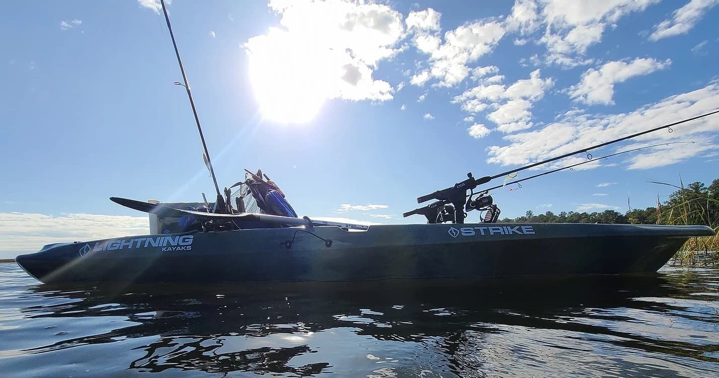 Kayak angler fishing on sunlit coastal waters near shoreline