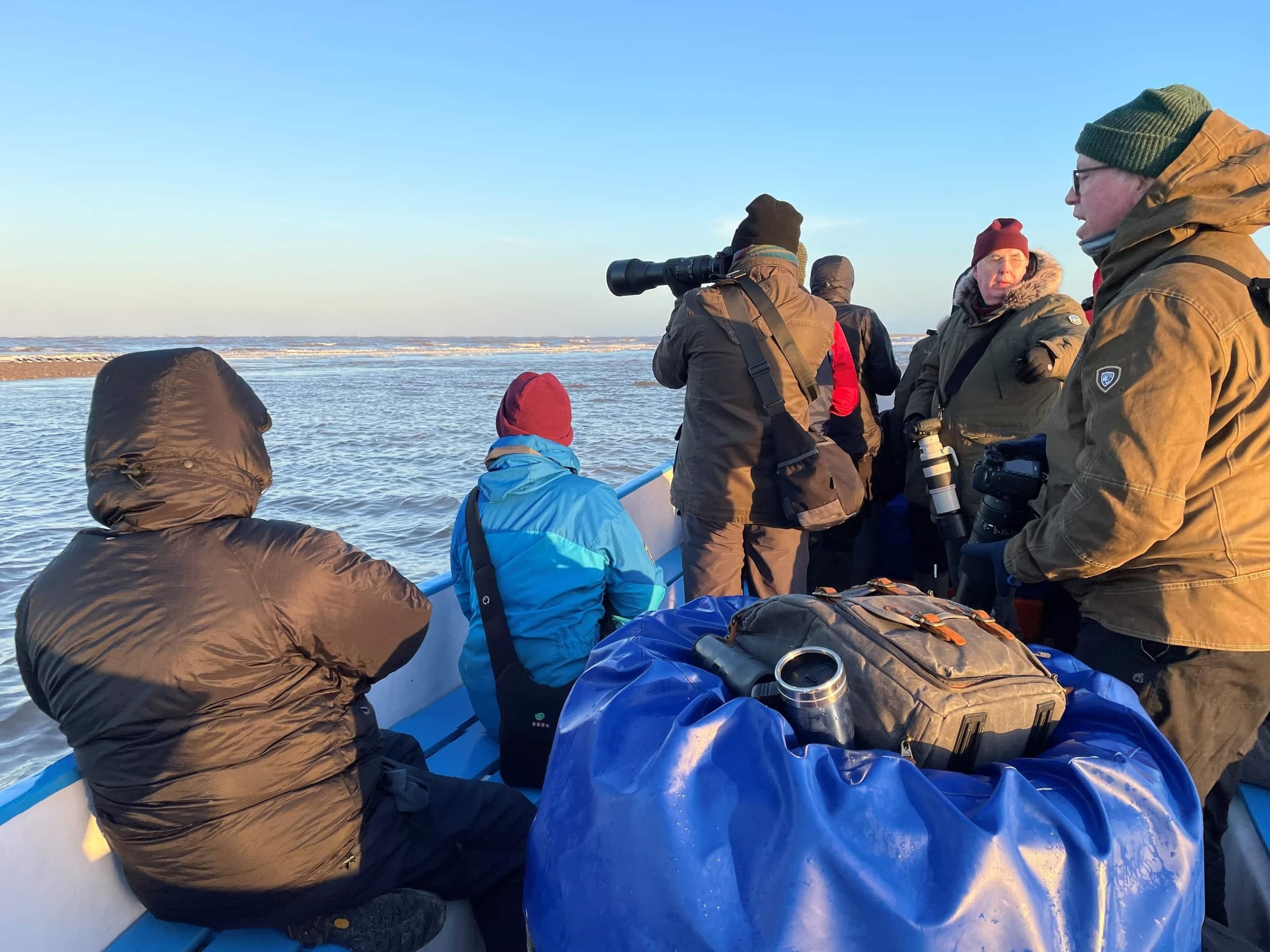 Birdwatchers and photographers on coastal boat during sunrise