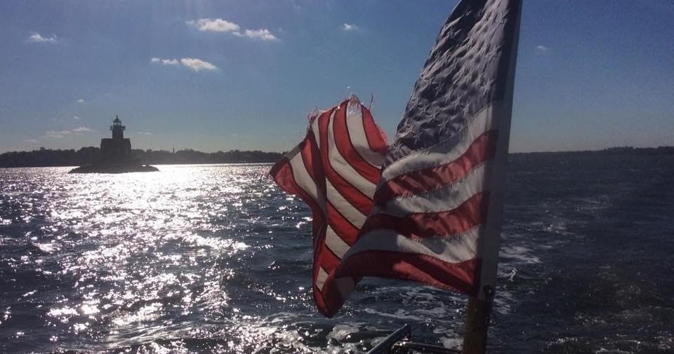 American flag flying from boat with lighthouse and sparkling sea