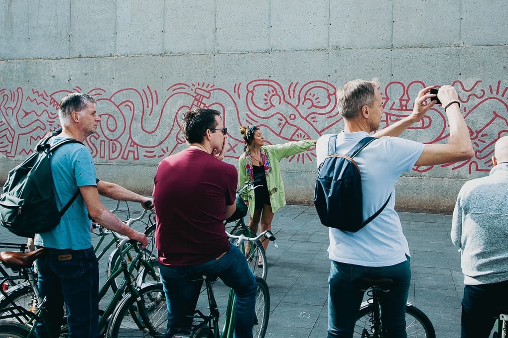 Urban bike tour group pausing by graffiti mural in Barcelona streets