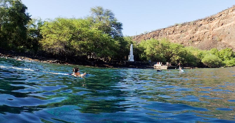 Snorkelers swimming near lush shoreline and volcanic bay in Hawaii