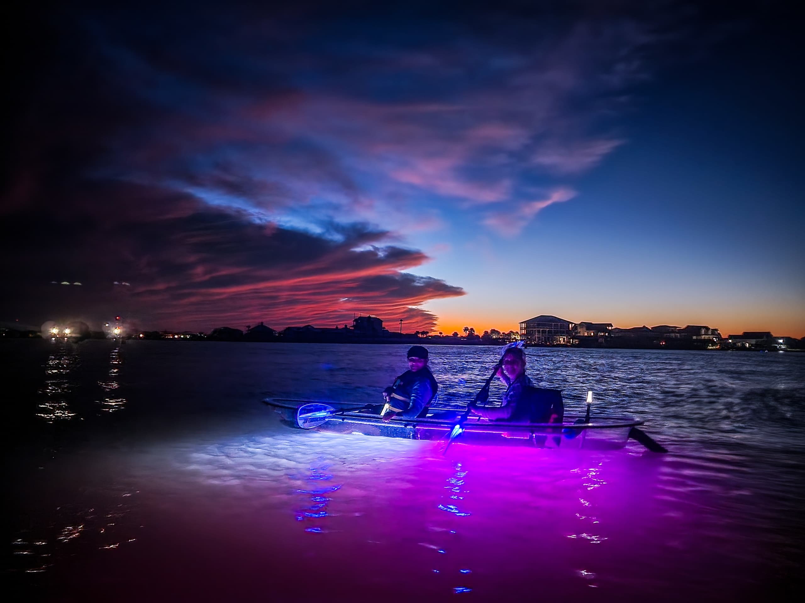 Two kayakers paddling at sunset over calm coastal waters