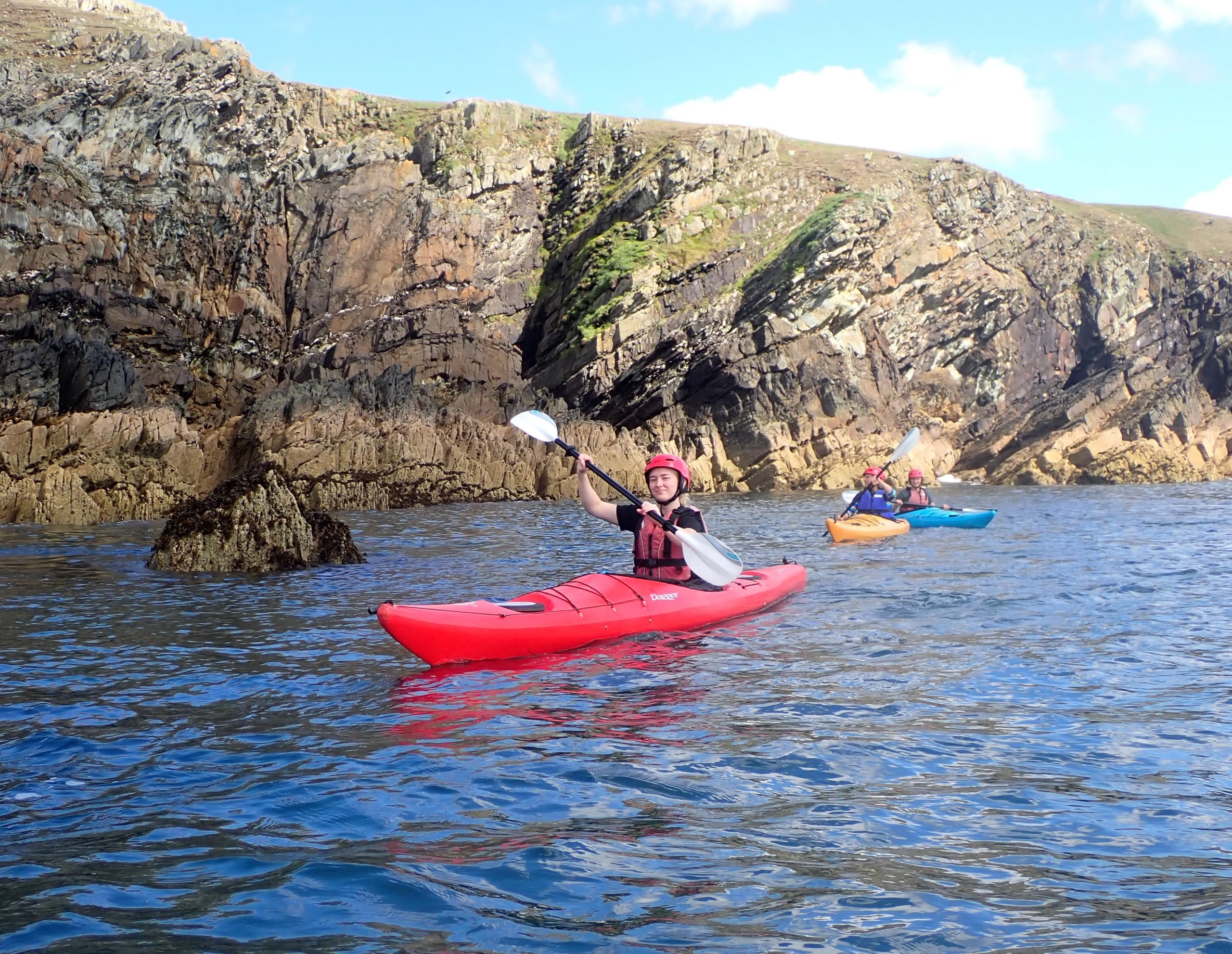 Kayaker paddling near dramatic coastal cliffs in calm sea