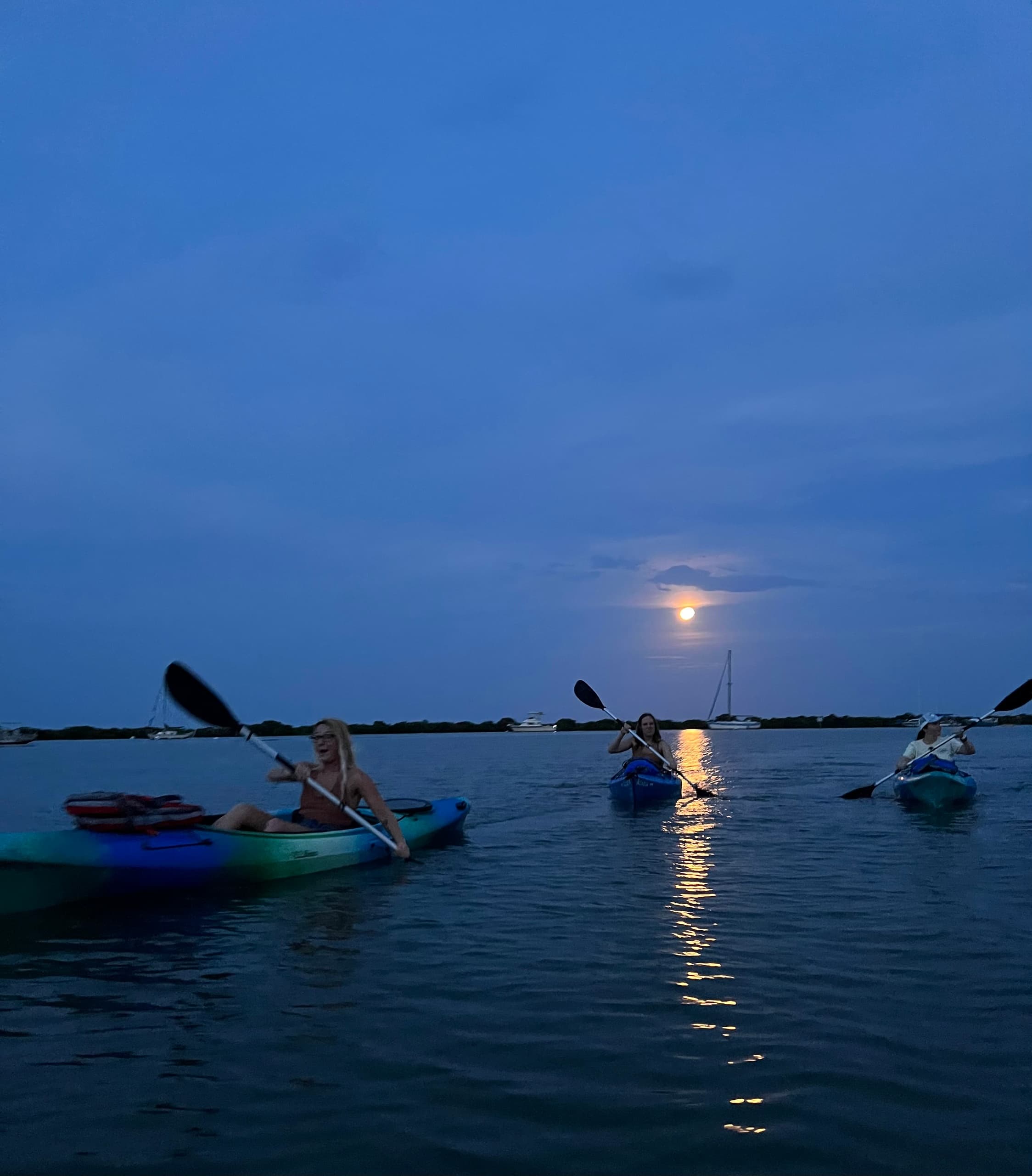 Kayakers paddling at moonlit coastal bay during sunset