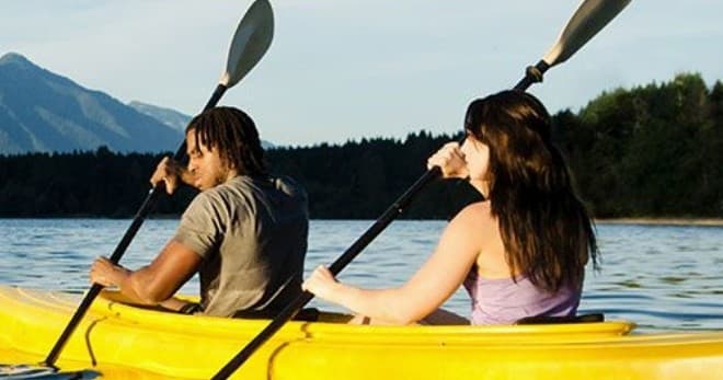 Two kayakers paddling a yellow tandem kayak on mountain lake
