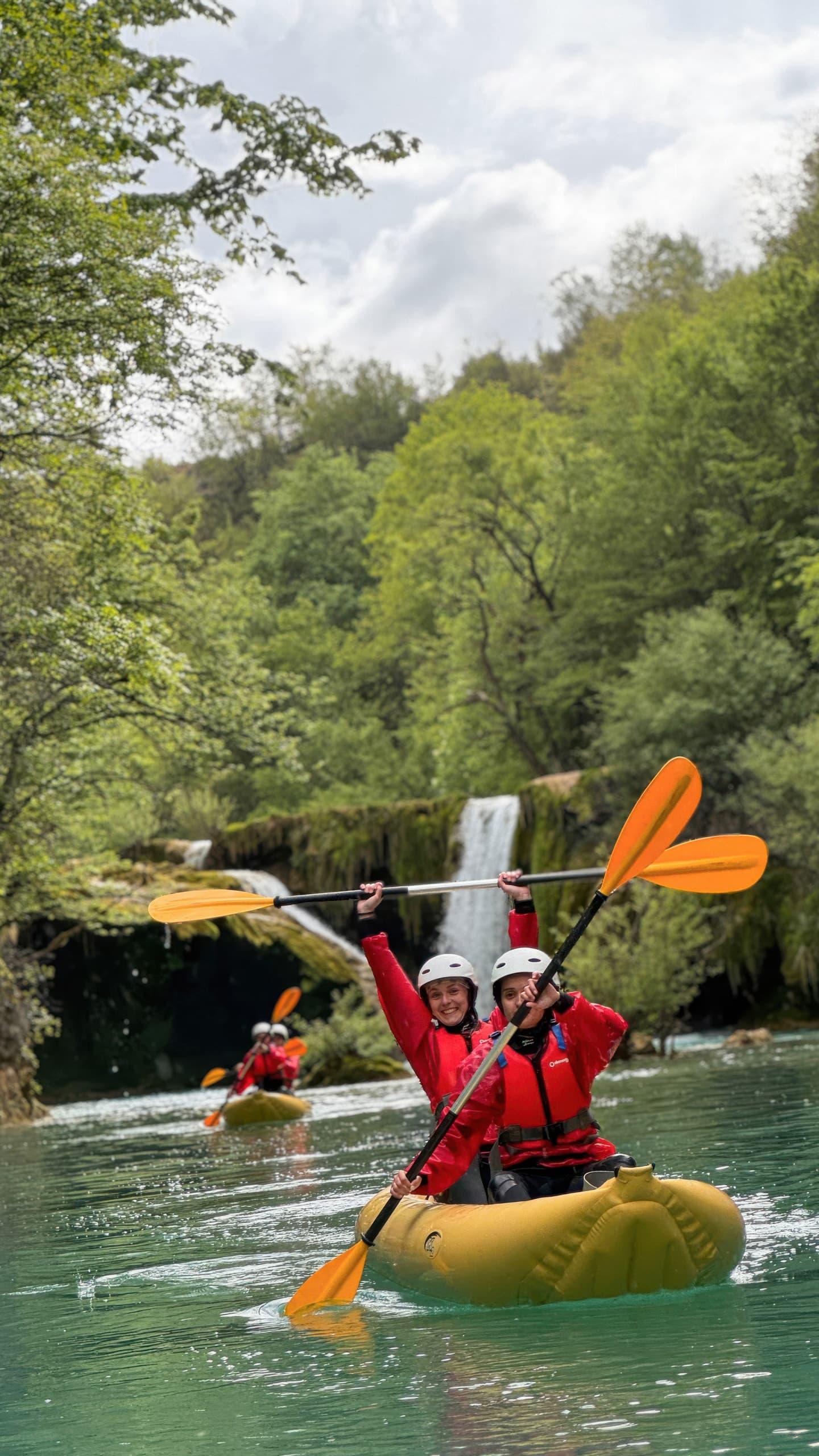 Kayaker raising paddle triumphantly on calm river near falls
