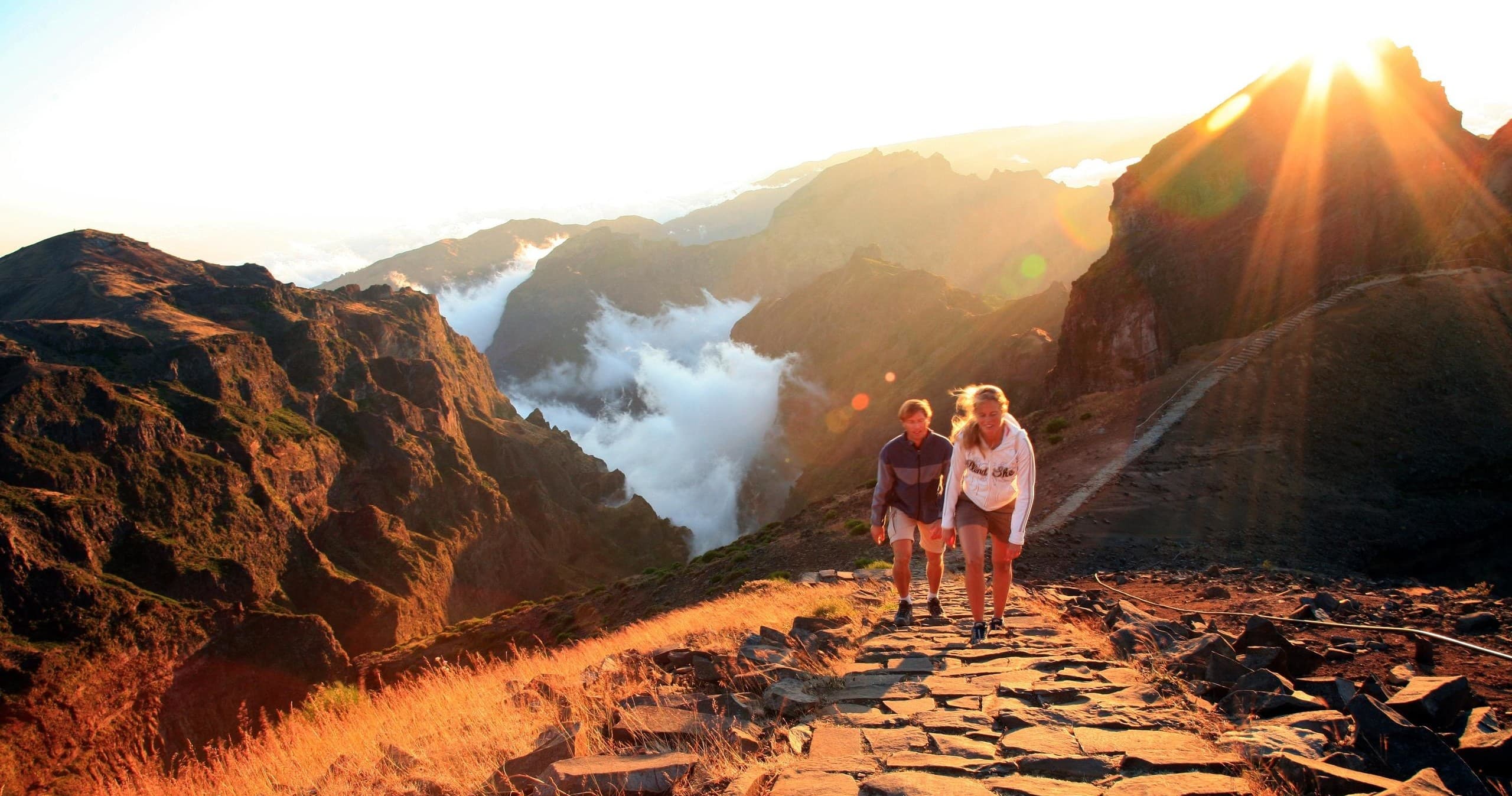Sunrise hikers on rocky mountain path overlooking misty valley