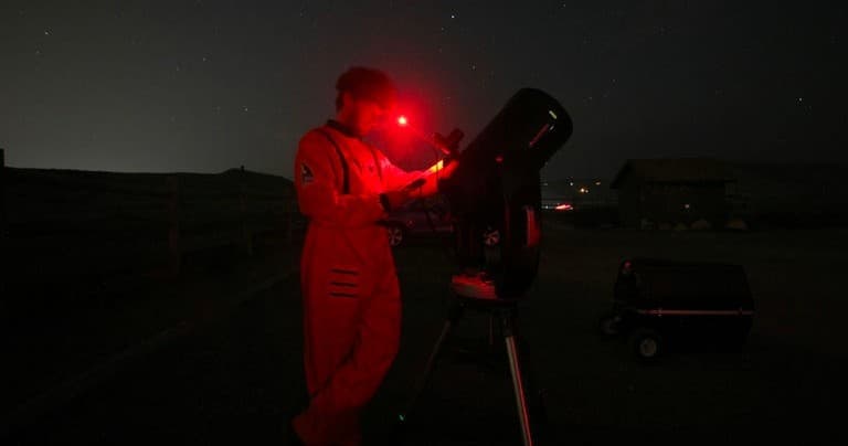 Astronomy enthusiast adjusting telescope with red headlamp outdoors