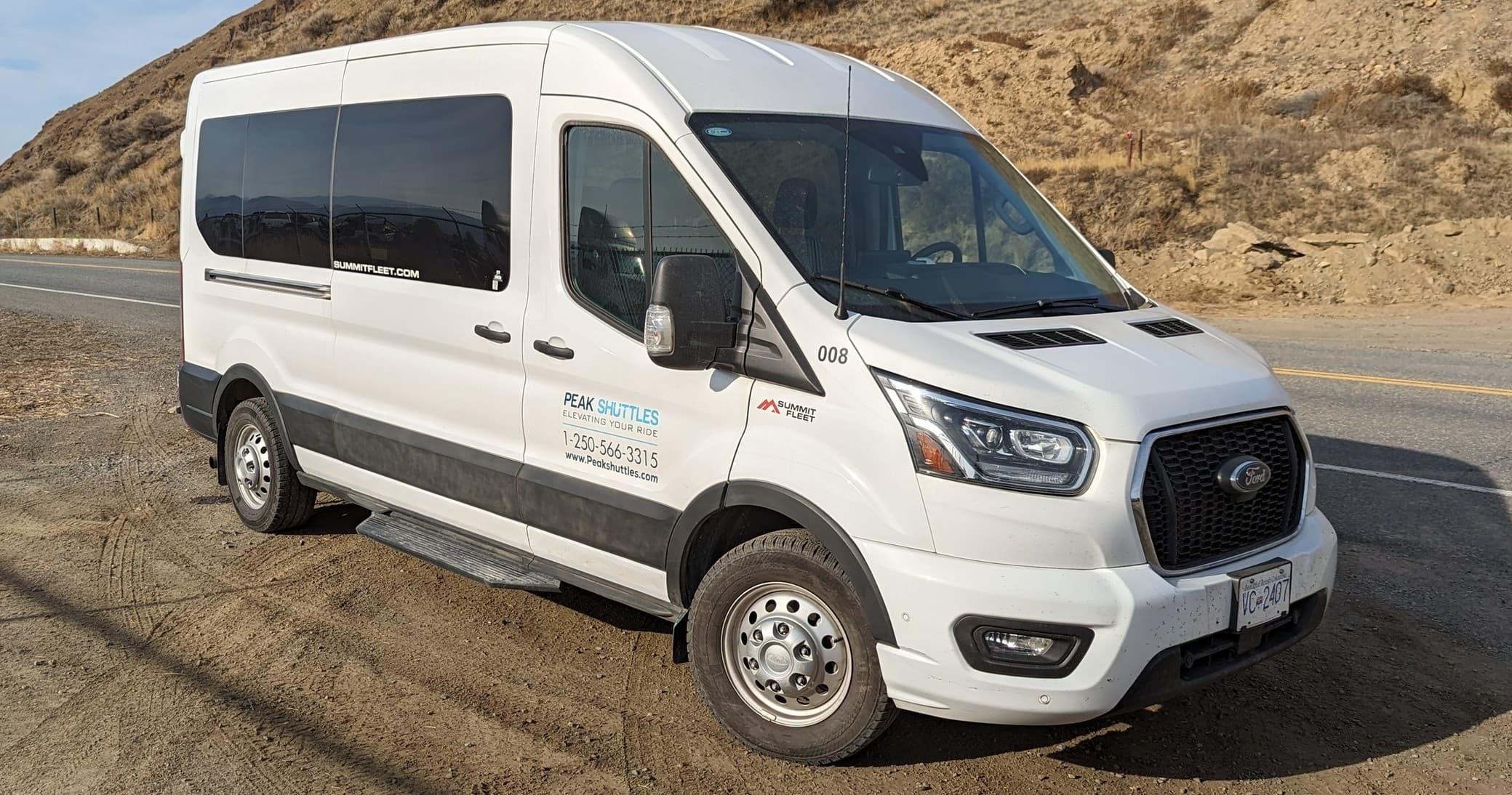 White shuttle van parked on desert road near rocky hills