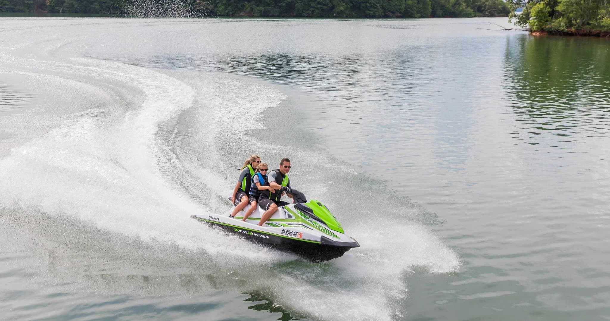 Jet ski riders carving across open lake creating water spray