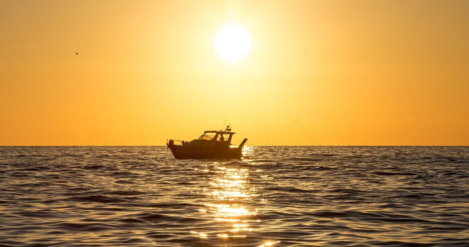 Sunset sea silhouette of small boat on calm golden water