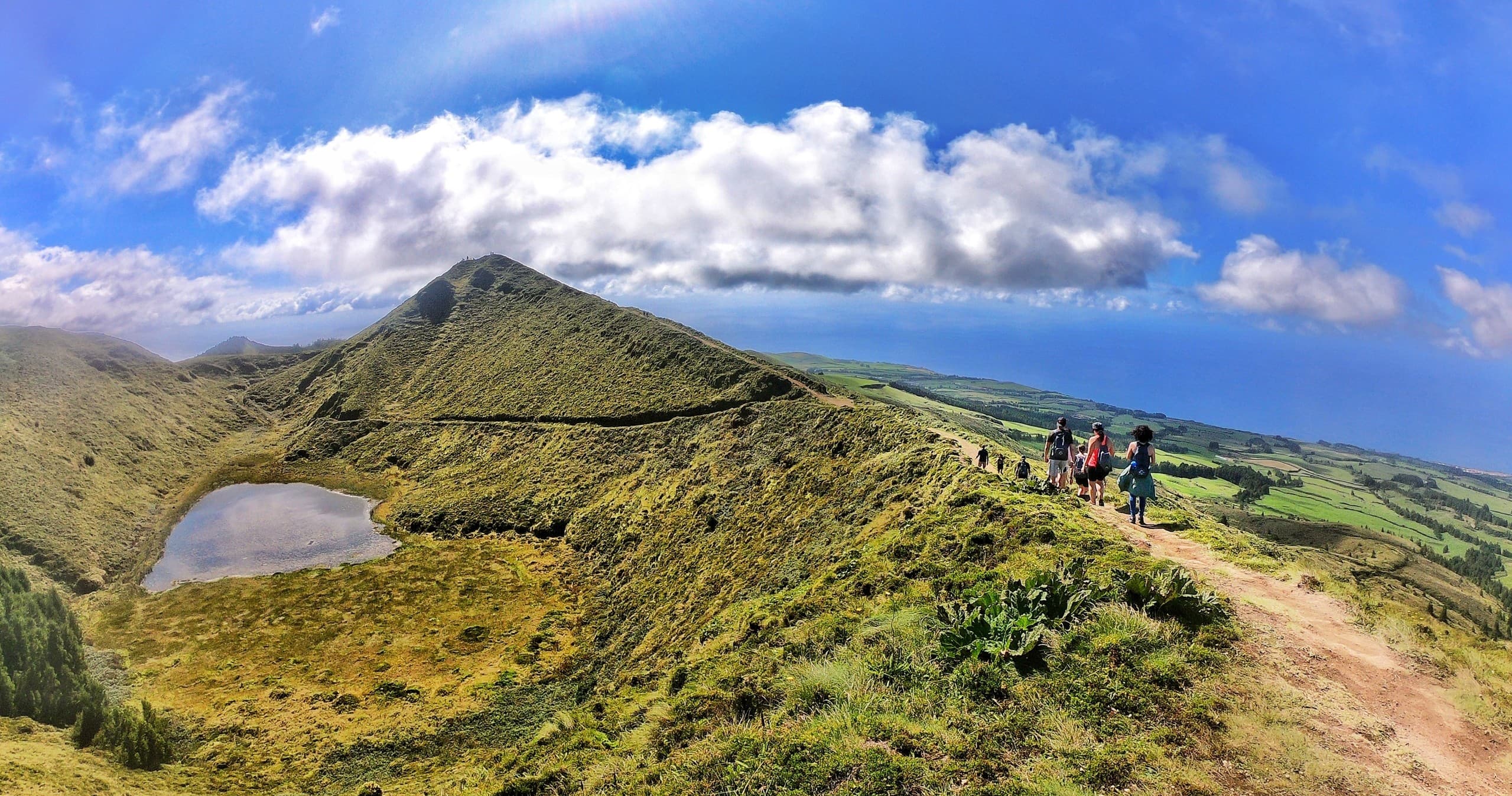 Hikers on volcanic ridge with lakes and rolling hills in Azores