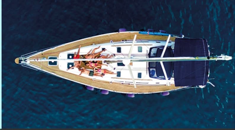 Aerial top-down sailboat tour with sunbathers on deck