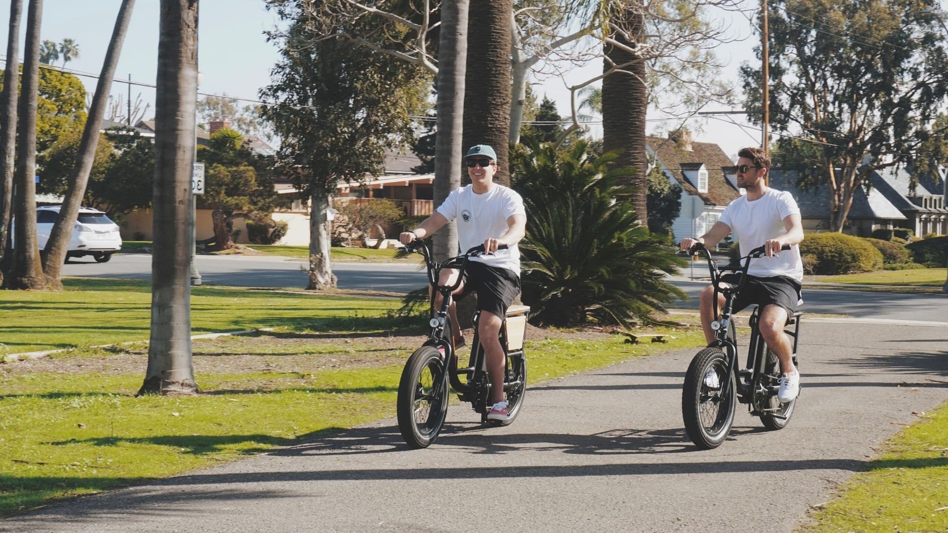 Two riders on electric bikes cruising a sunny coastal park path