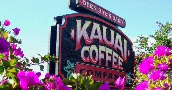 Kauai Coffee company sign with tropical flowers at farm entrance