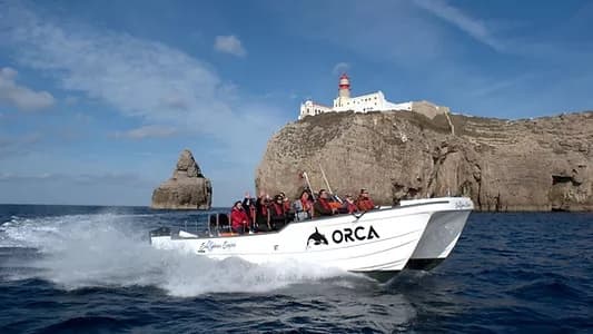 Tour boat cruising past Sagres lighthouse and rugged sea cliffs
