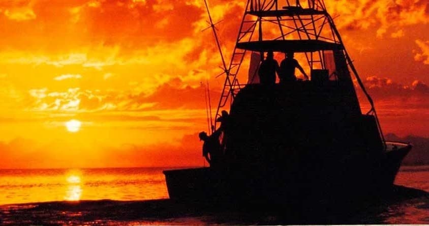 Fishing boat silhouetted at vibrant ocean sunset, offshore