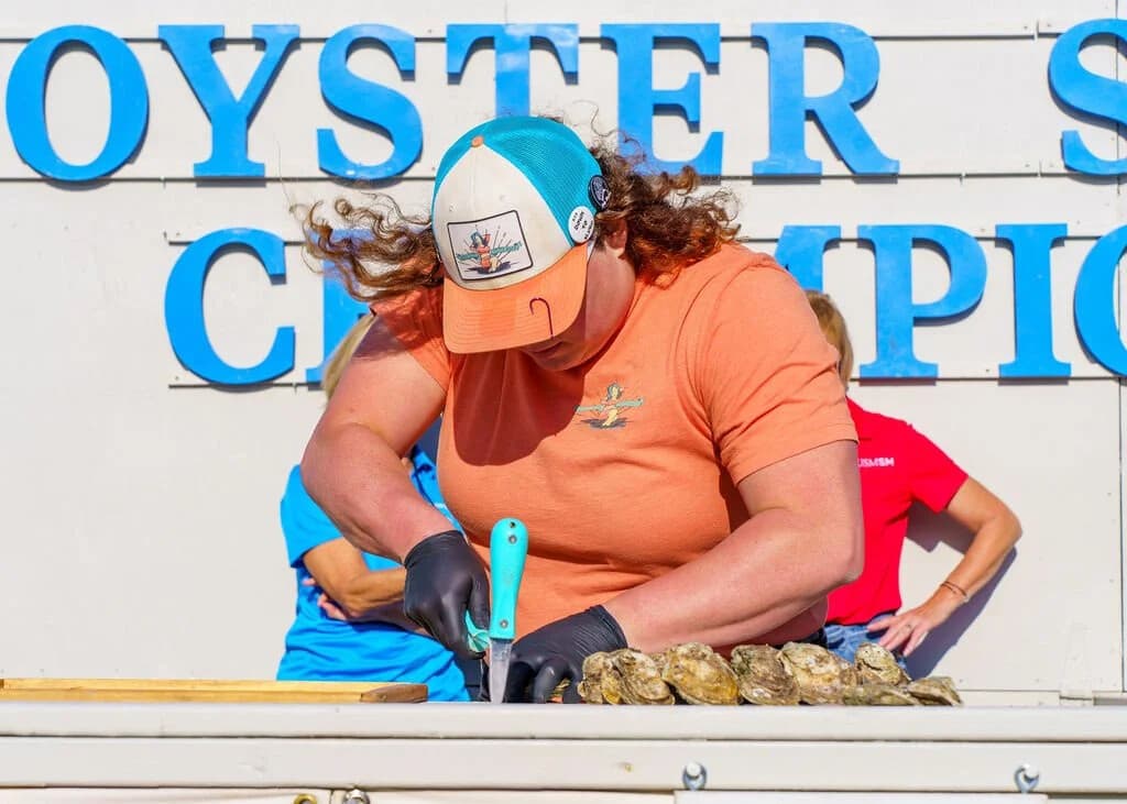 Woman shucking oysters at outdoor oyster festival competition sign