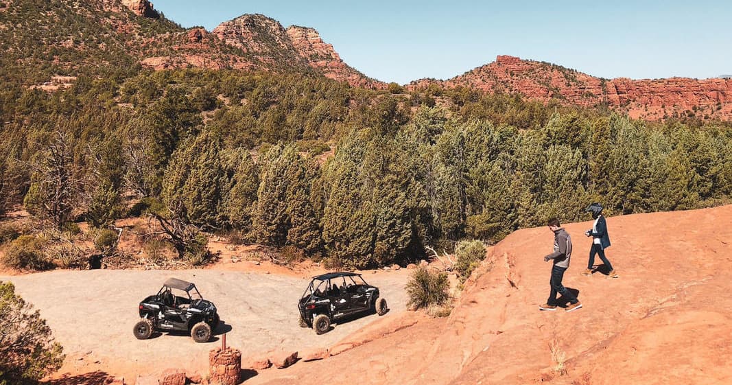 Off-road UTVs parked on red rock canyon trail with riders