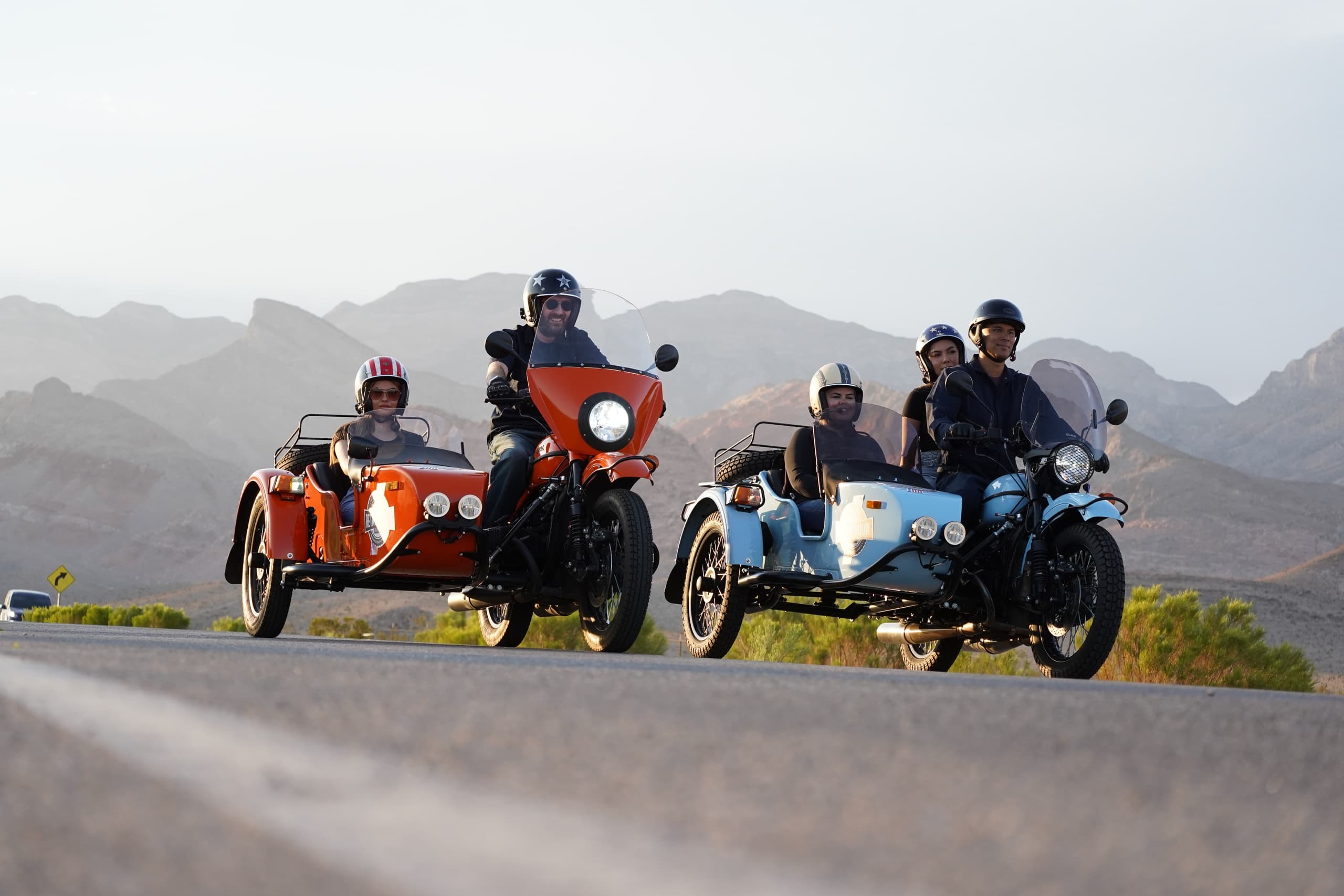 Two motorcycle sidecar tour riders on desert highway near mountains