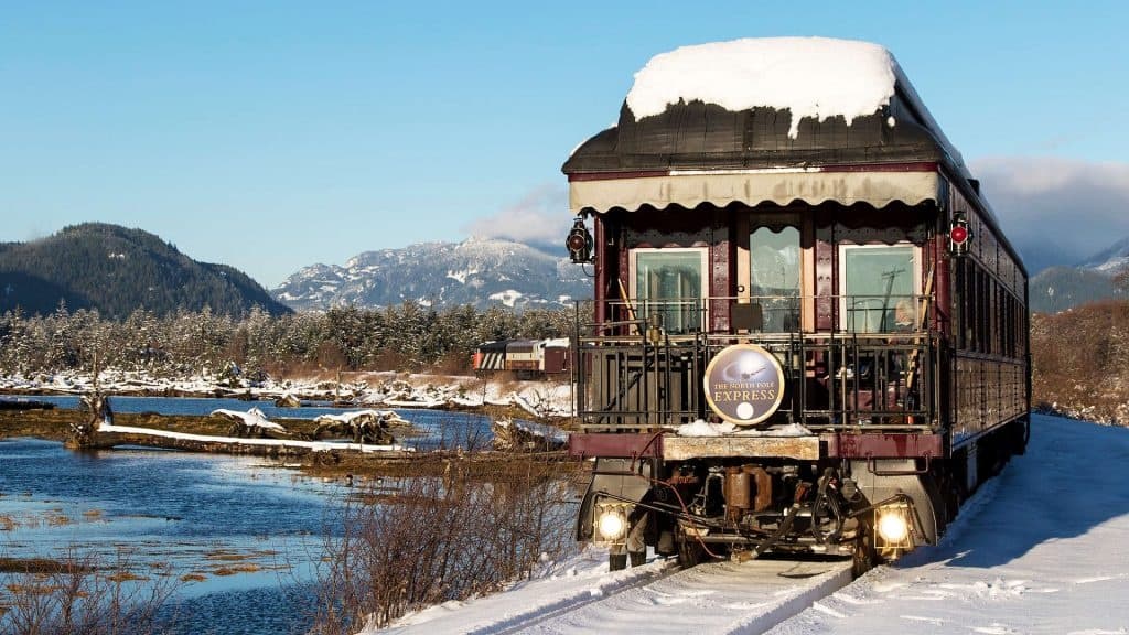 Heritage train running through snowy riverside mountains in BC