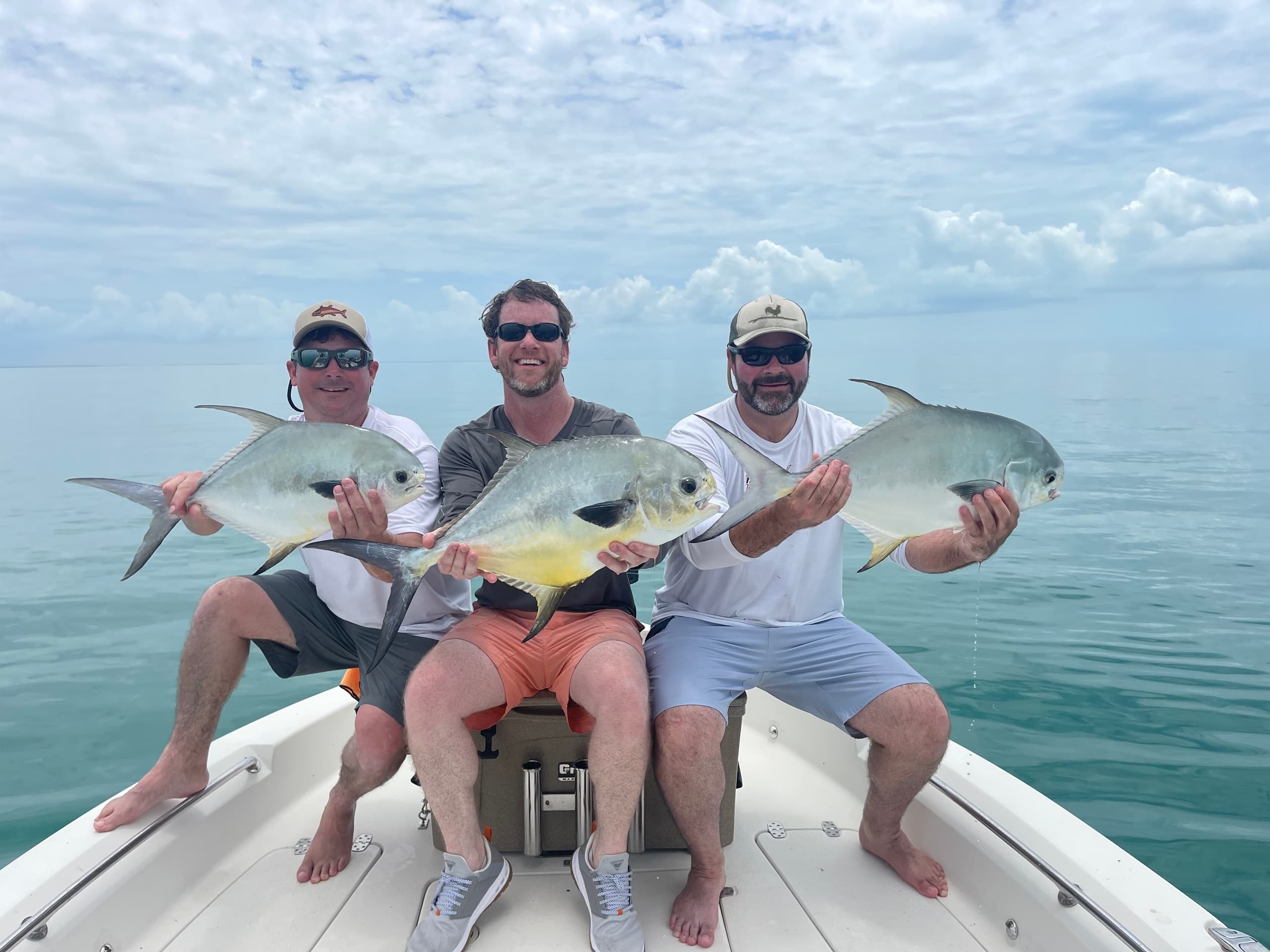 Three anglers holding pompano on a boat in Florida Gulf waters