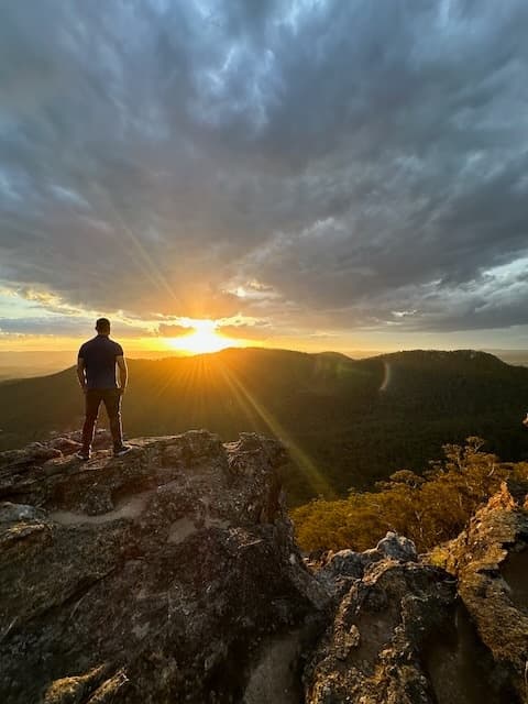 Hiker standing on cliff at sunrise, panoramic mountain viewpoint trek